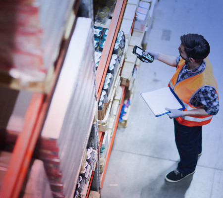 Ein Mann mit blau kariertem Hemd und orangefarbener Warnweste scannt Produkte in einem großen Lageregal. Die Simba ERP Software ist die optimale Unterstützung in der Material- und Produktionsplanung.